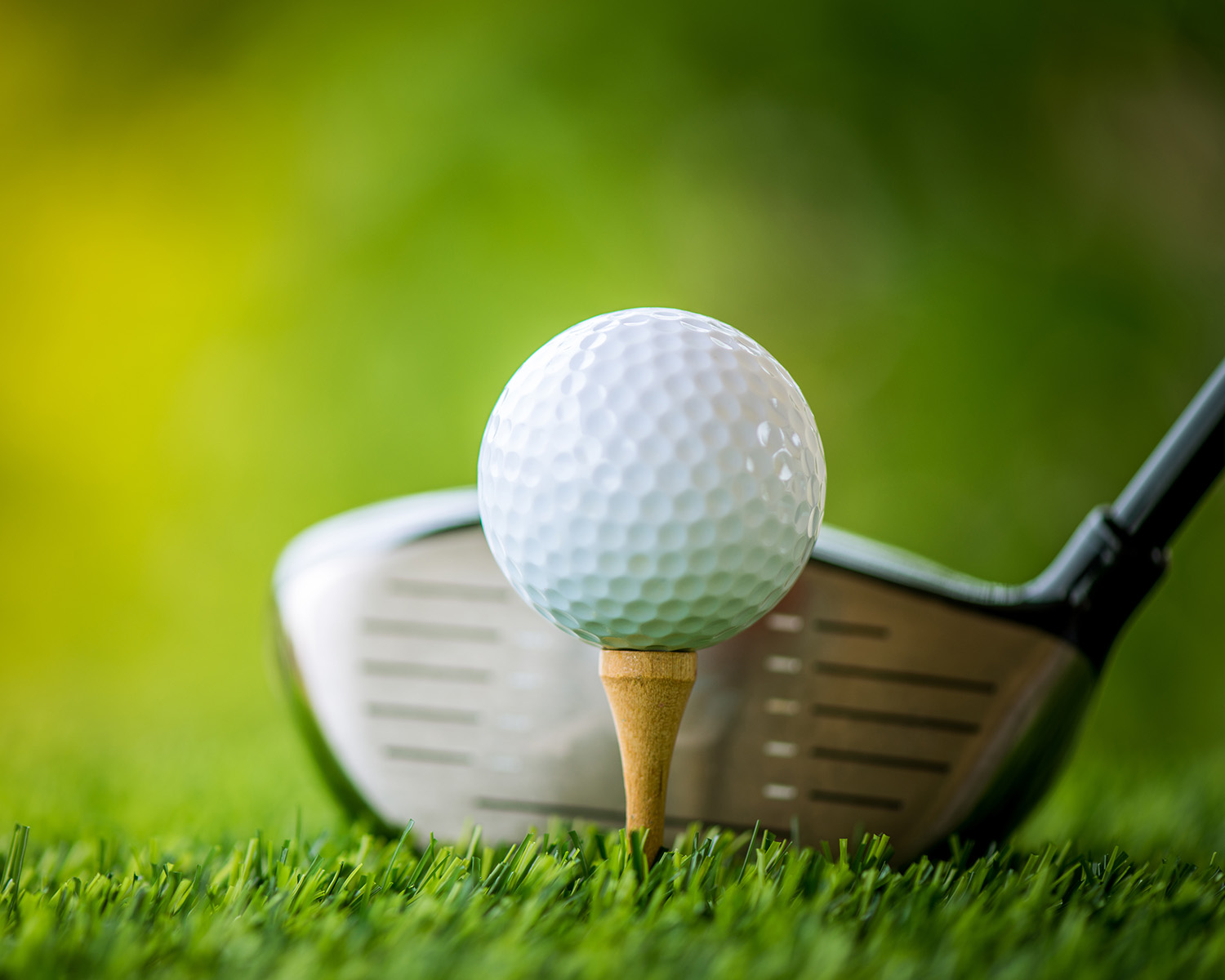 Golf club and ball on tee with green grass.