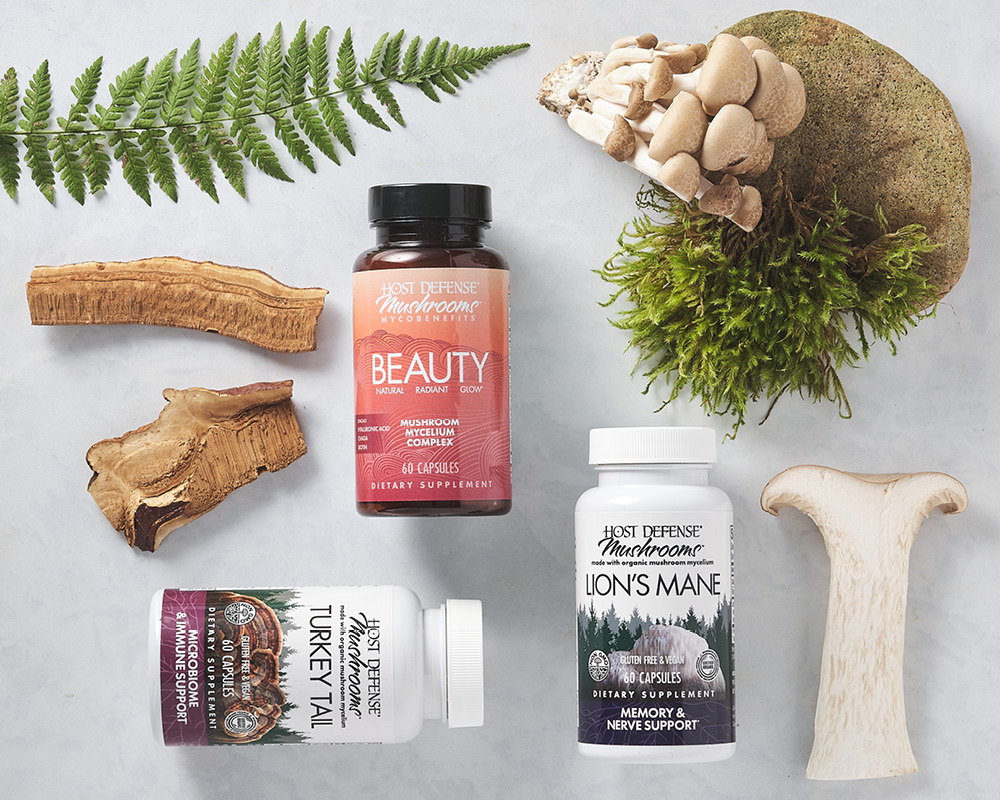 Three mushroom capsule bottles styled with real mushrooms, moss, a rock, and a fern