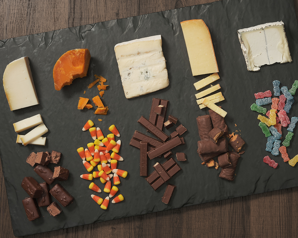 Five cheeses and five candies lined up on a slate board