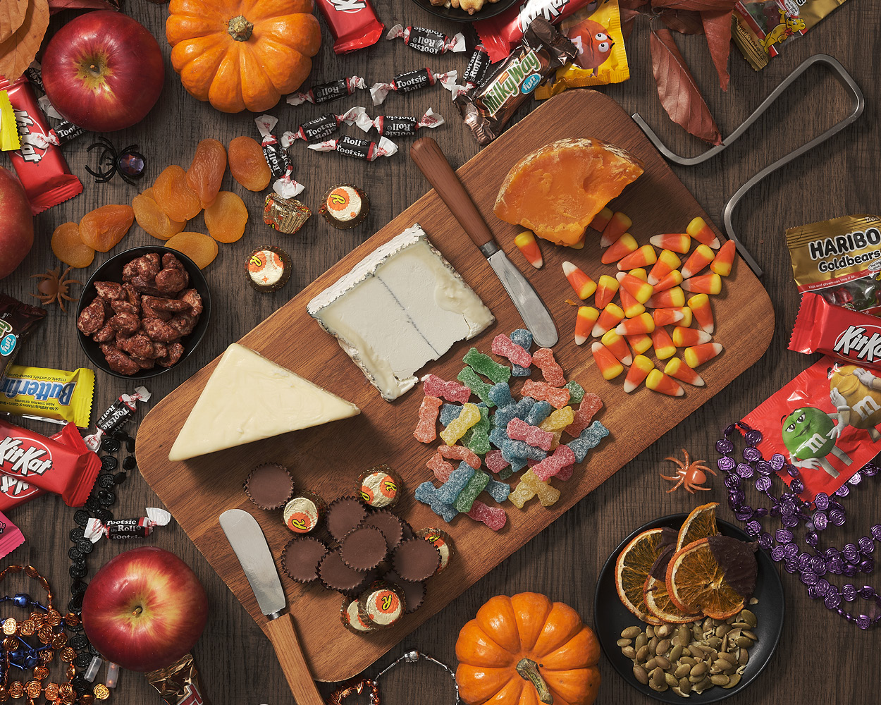 Charcuterie board of candy and cheeses surrounded by pumpkins, apples, and Halloween party favors