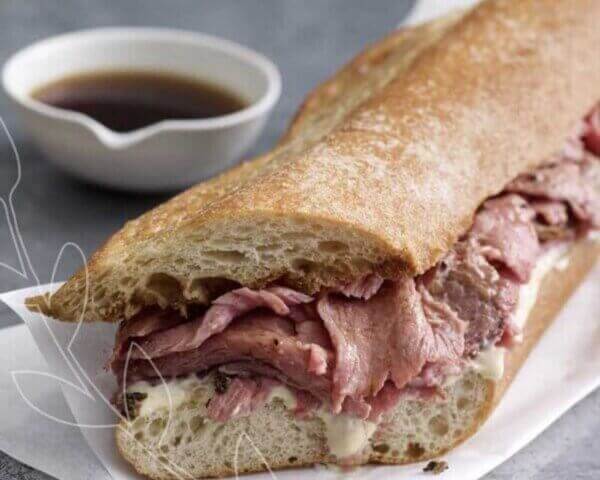 Close up shot of prime rib sandwich with au jus in the background.