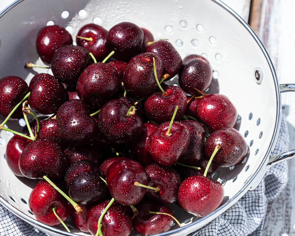 Deep red cherries in a white colander bowl.