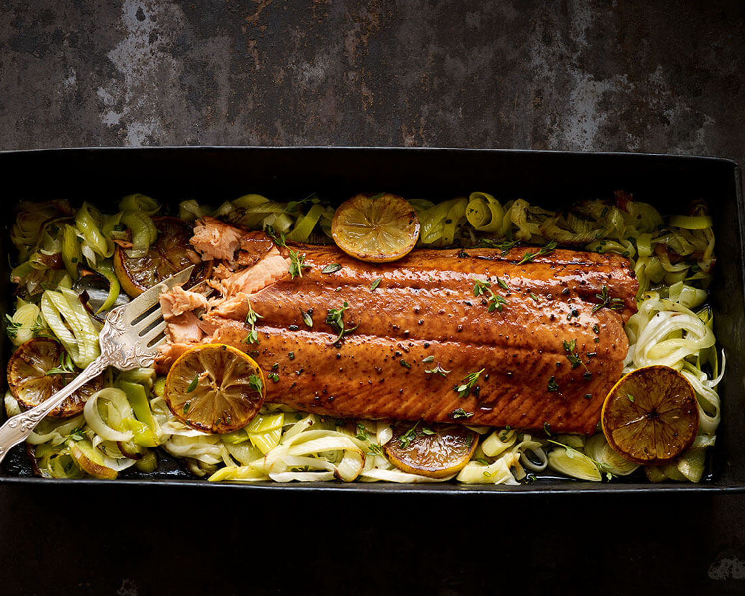 Serving dish with a large salmon fillet on a bed of vegetables.