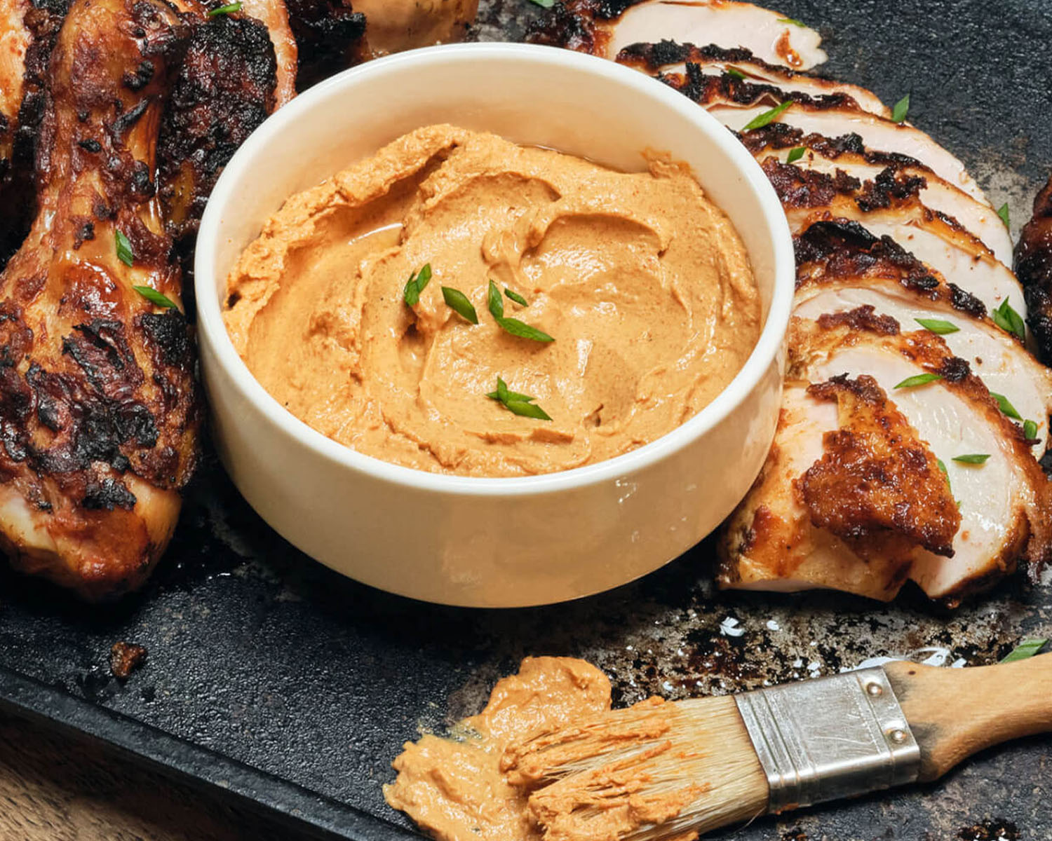 Thick marinade in a bowl on a tray with sliced meat.
