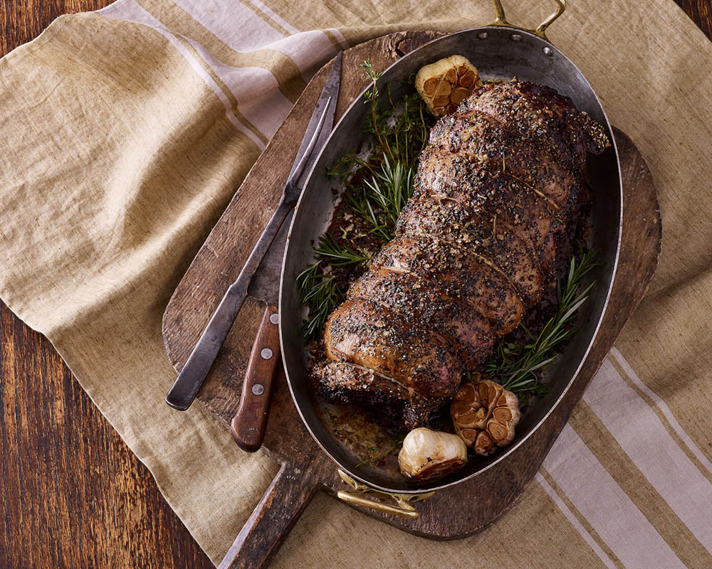 Cooked lamb roast in a pan with sage and garlic