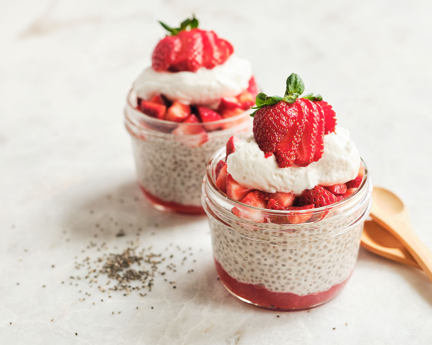 Two jars with strawberry chia seed pudding topped with fresh strawberries and whipped cream.