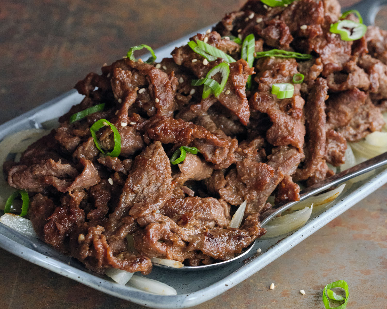 Thin sliced beef piled high on a tray, garnished with green onion.
