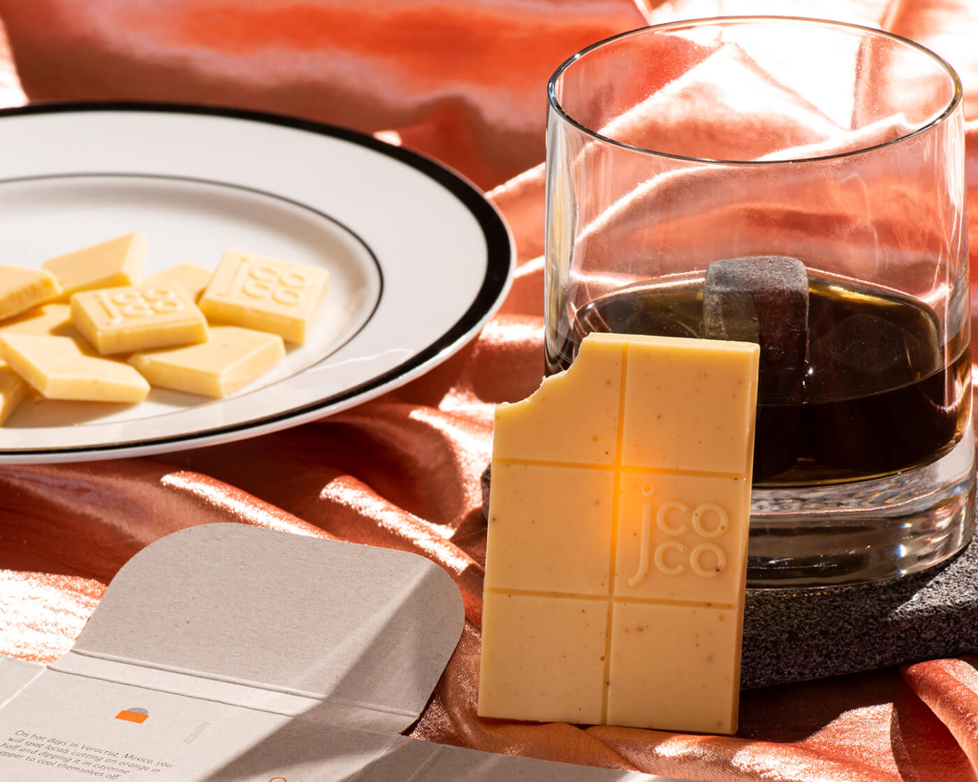 chocolate pieces on a plate and a white jcoco chocolate bar with a glass of scotch