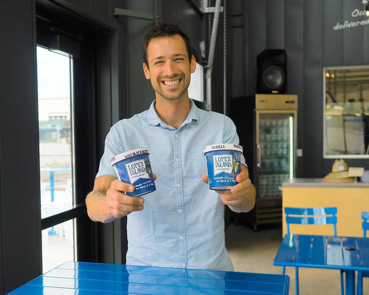 Alex Thieman holding two pints of Lopez Island Creamery Ice Cream in his scoop shop in Anacortes 