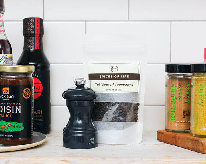 Package of peppercorns and a pepper grinder on a pantry shelf.