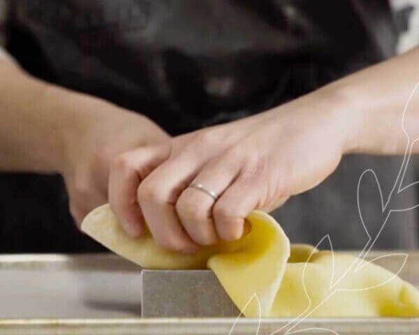 A baker's hands placing a pastry sheet into a pan.