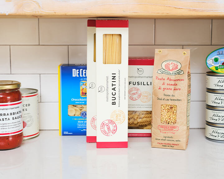 Pasta, sauce, and cans on a pantry shelf.