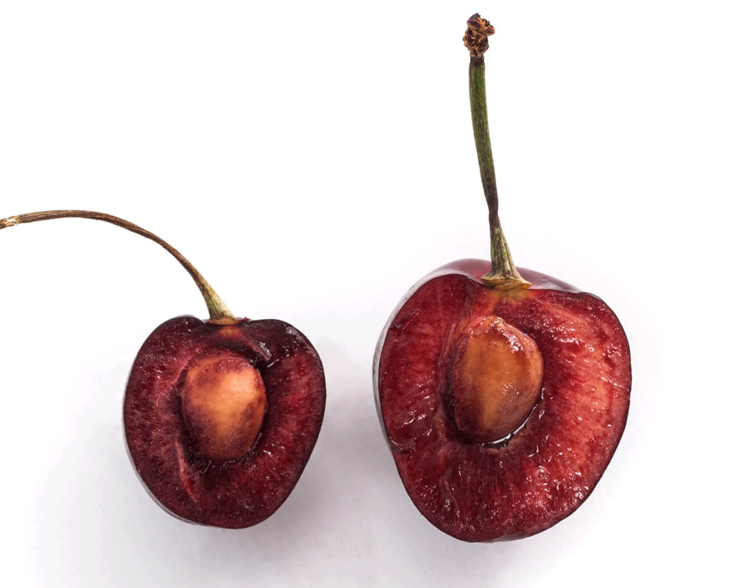 Two red cherries sliced open to show the pit.