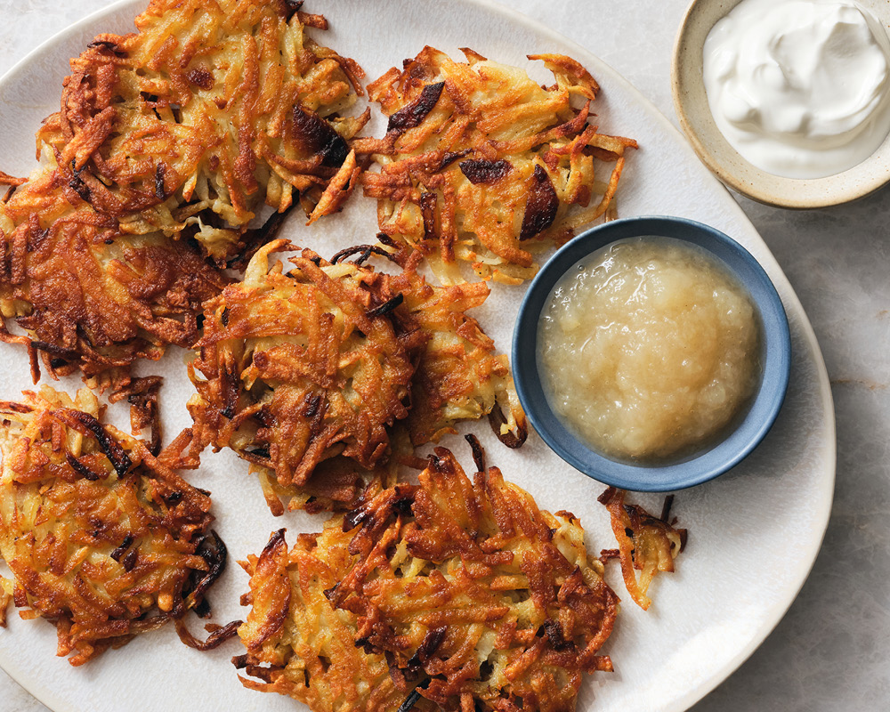 Latkes on white plate with sides of applesauce and sour cream