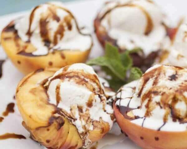 Roasted peaches filled with vanilla ice cream, drizzled with balsamic vinegar, and garnished with mint leaves.