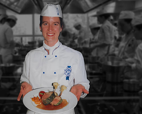 Lindsay Gott in a chef's uniform holding a plate of food.