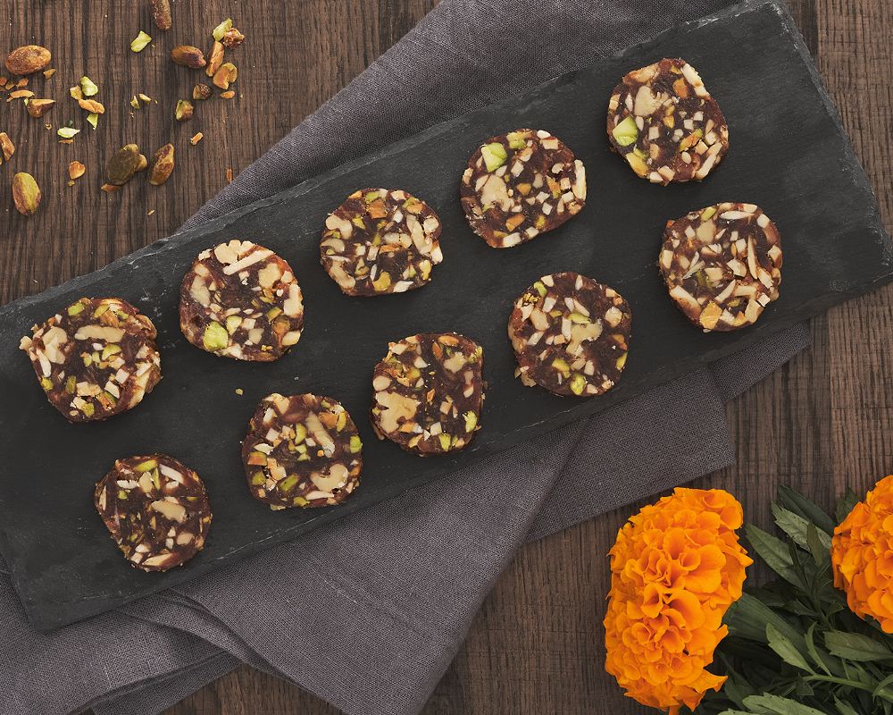 Date and nut discs on a slate serving tray surrounded by nuts and flowers