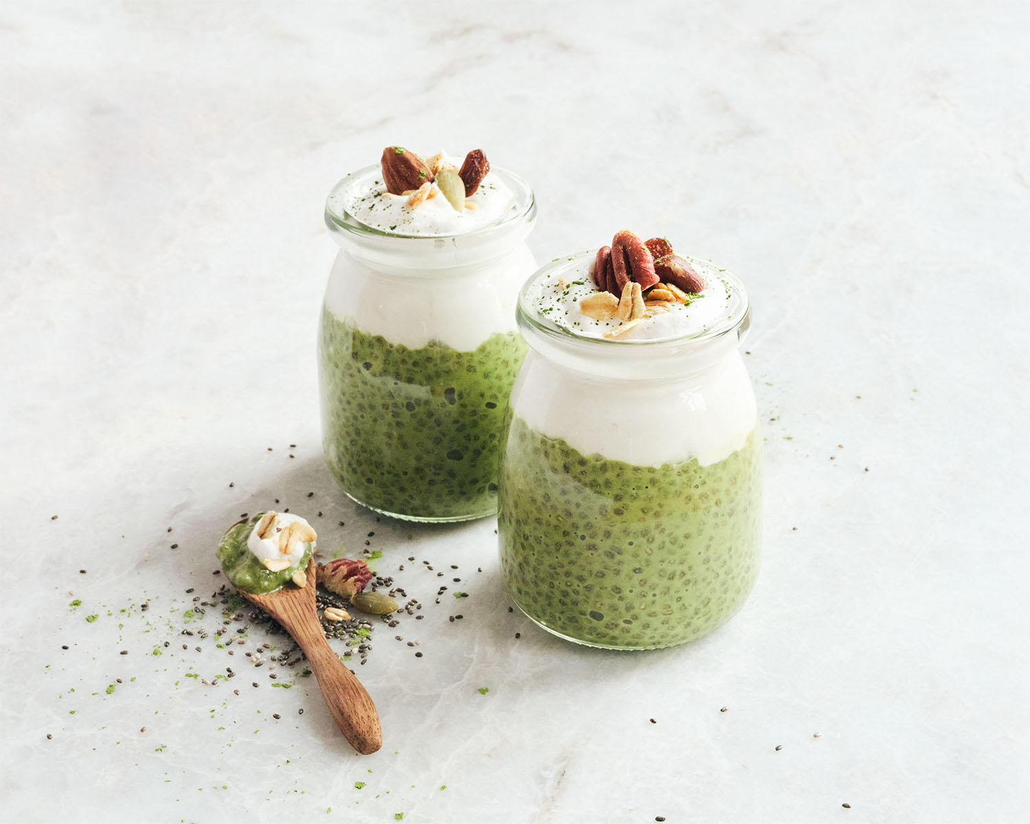 Two small jars filled with green matcha chia seed pudding, topped with whipped cream and nuts.