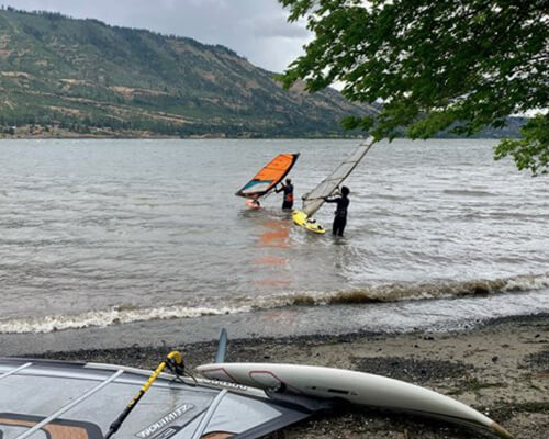 Two people walking into a lake to go wind surfing.