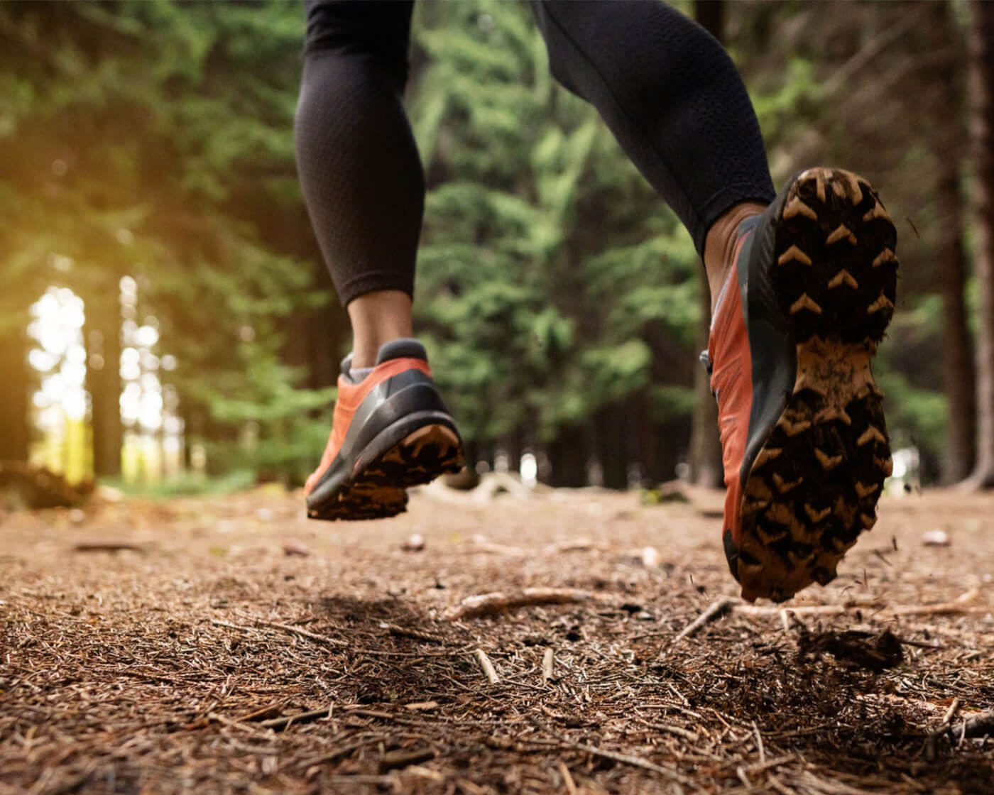 Pair of feet wearing running shoes, running on a trail surrounded by trees