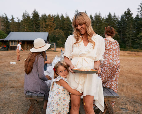 Audra Lawlor smiling down at her little daughter who is hugging her leg.