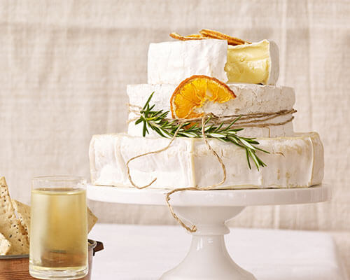 Three wheels of cheese stacked like a wedding cake, decorated with dried citrus and herbs