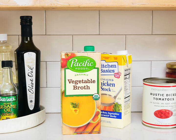 Packages of vegetable and chicken broth on a pantry shelf.