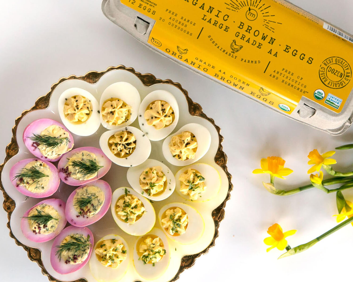 deviled eggs on a plate with egg carton and flowers