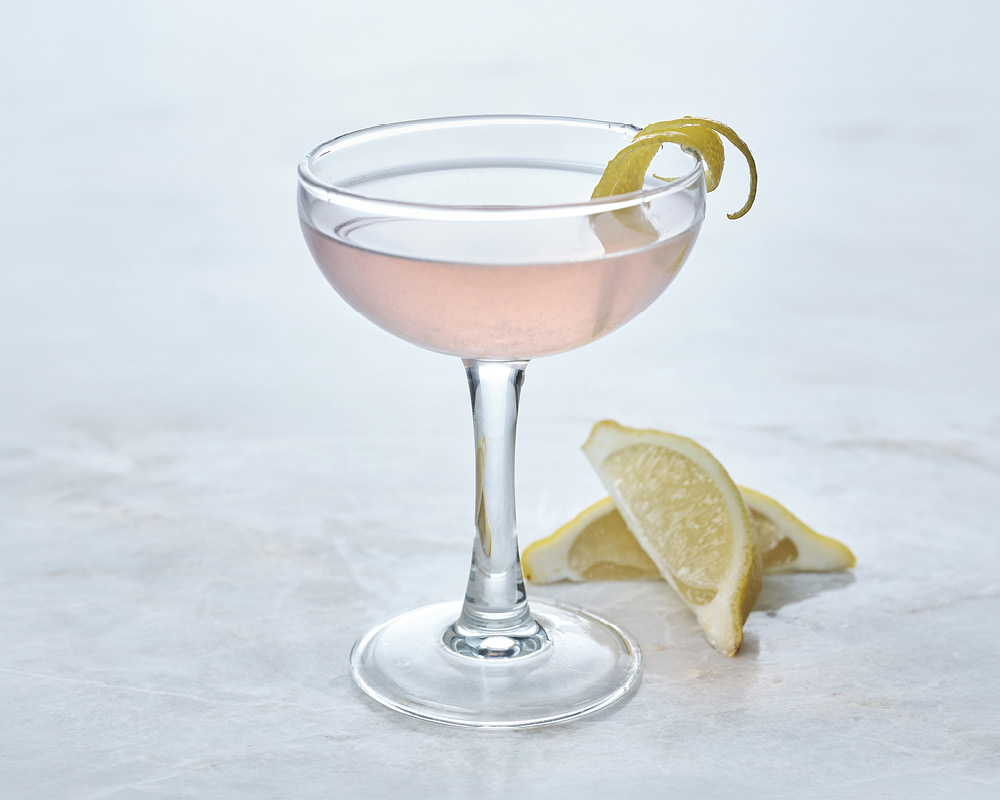 Empress 75 Cocktail with lemon garnish on white gray background