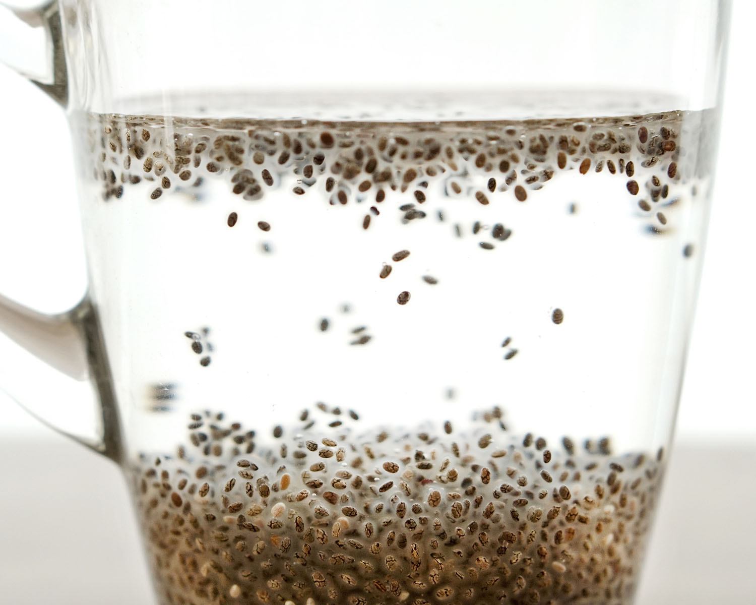 Chia seeds floating in water in a clear glass mug.