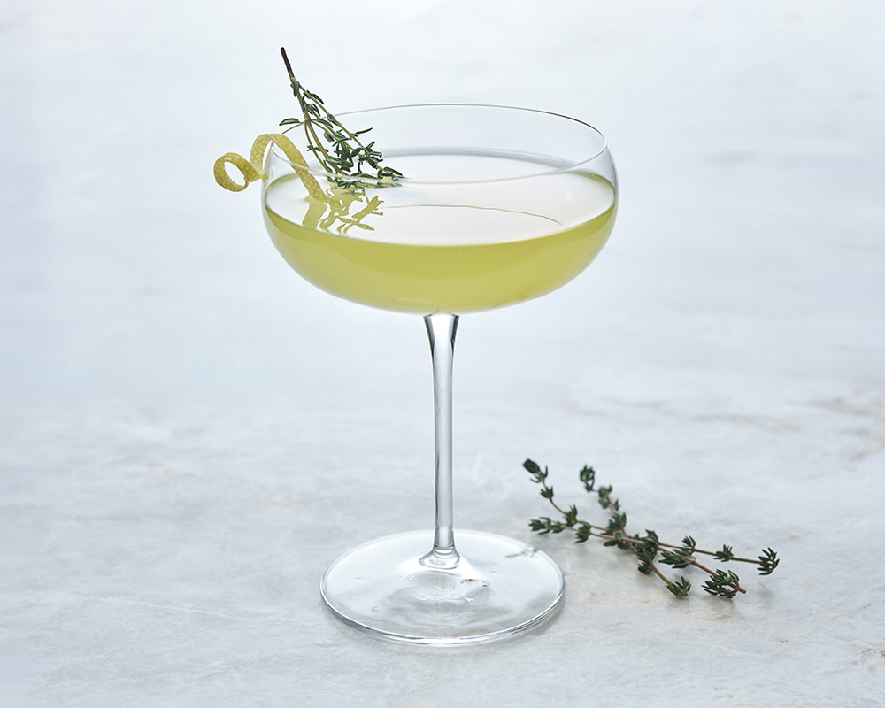 Lemon tuxedo cocktail with thyme and lemon garnish on white gray background