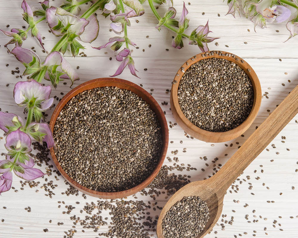 Two small wooden bowls and a spoon filled with chia seeds