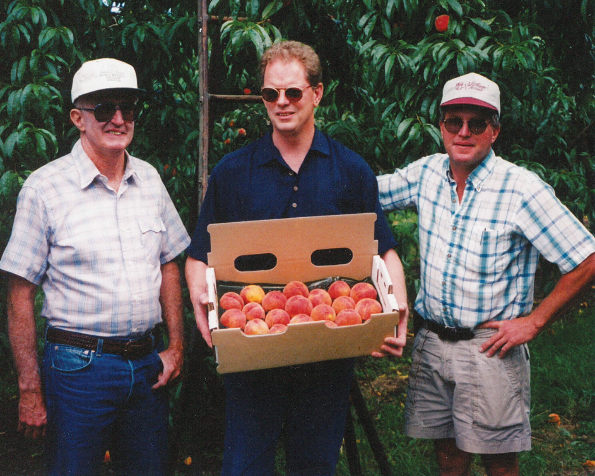 Our founder holding a box of peaches with two people