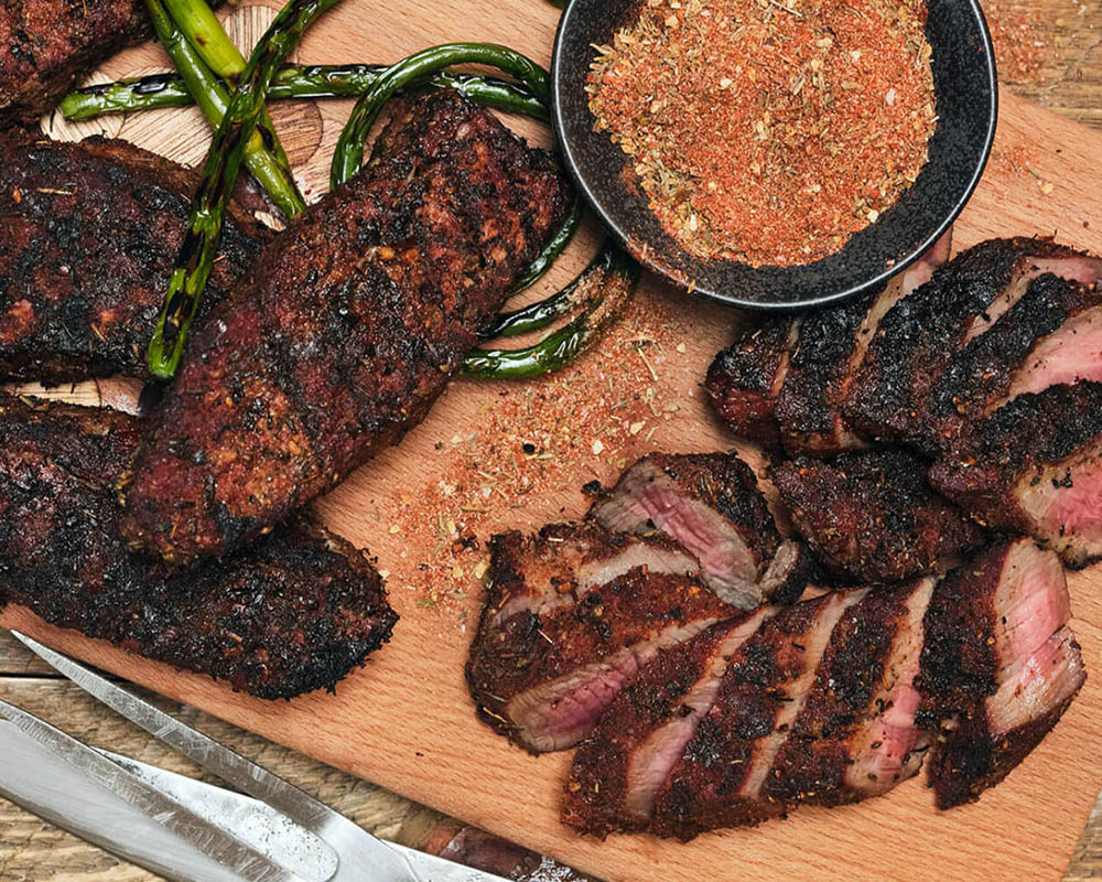 Sliced meat on a tray with a bowl of spice rub.