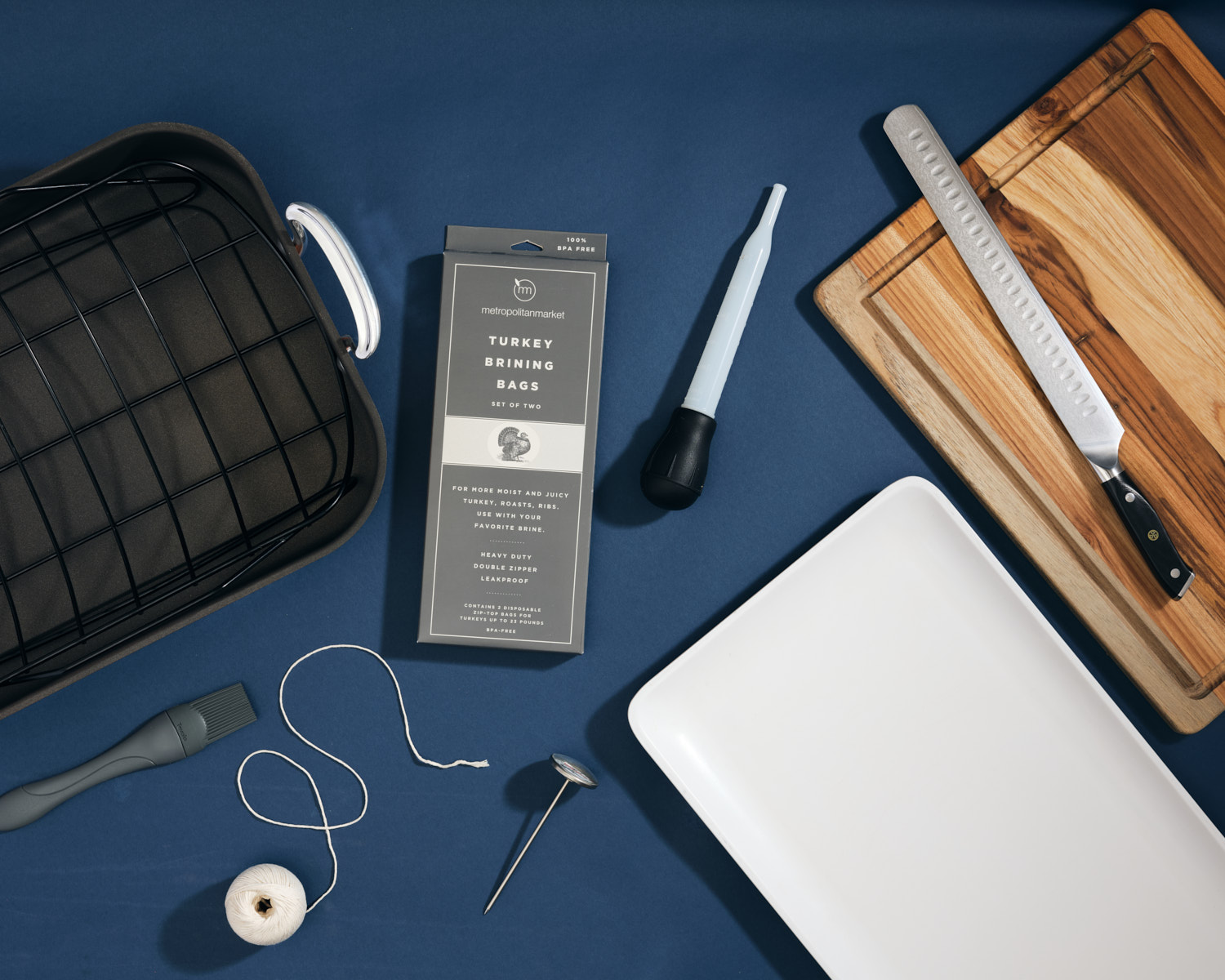 Roasting pan, thermometer, turkey bag, baster, brush, serving platter, cutting board, and carving knife on a blue background