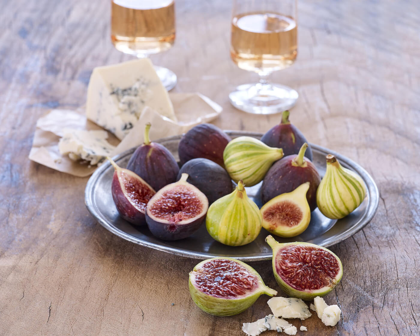 a variety of figs on a plate with blue cheese and wine glasses