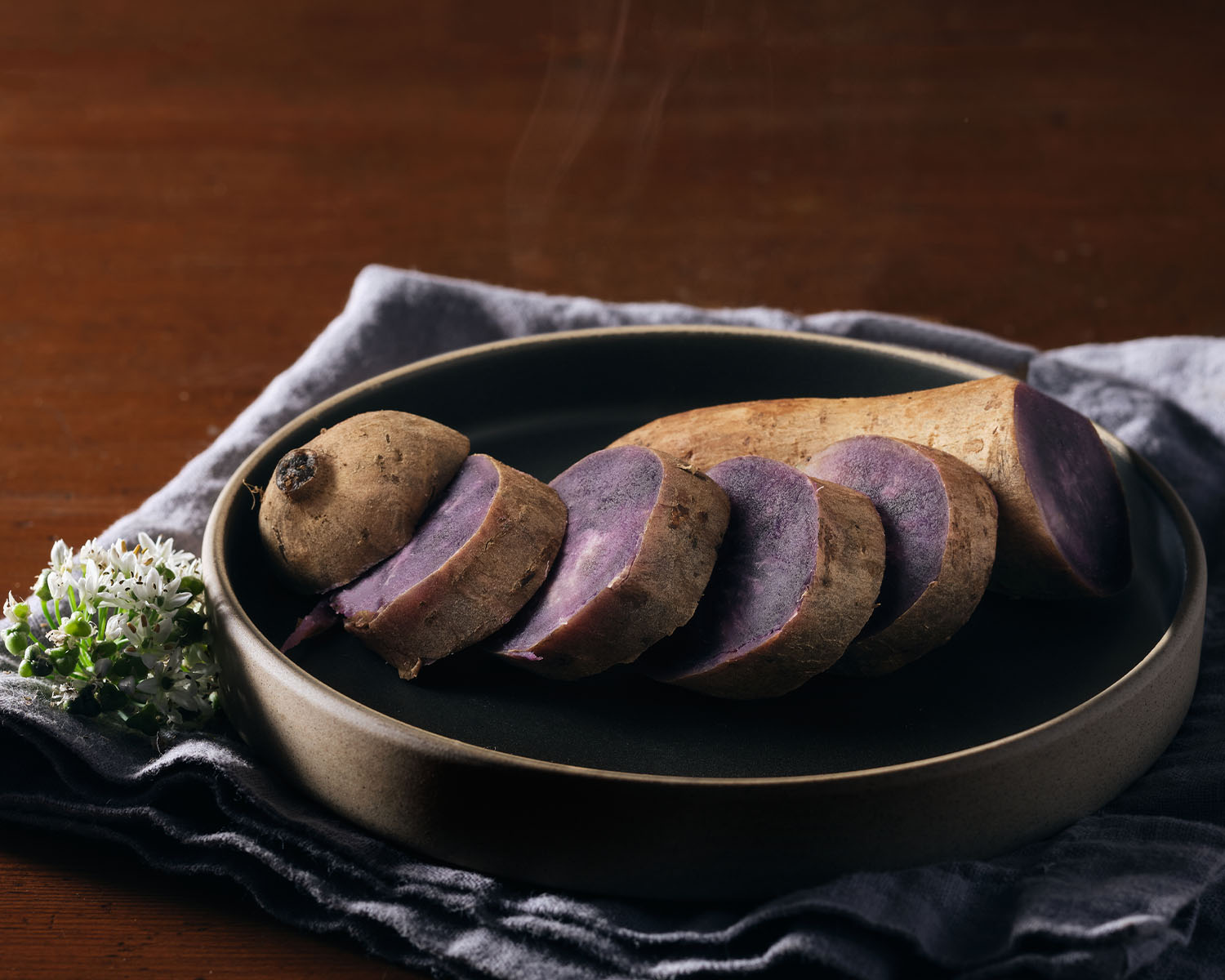 Dark bowl with a sliced purple sweet potato on a wood table.