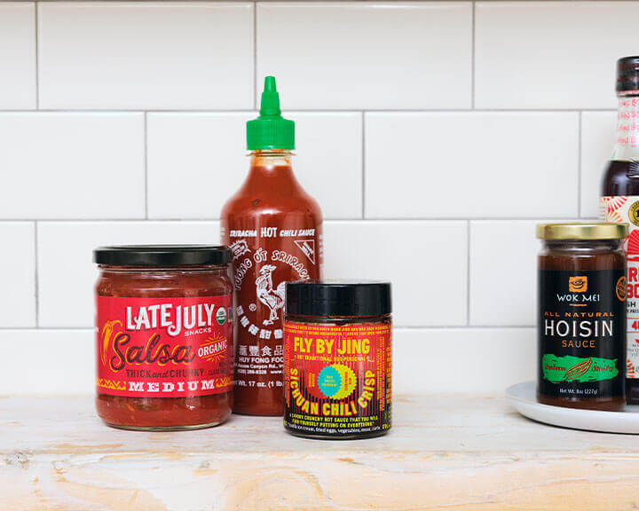 Salsa, Sriracha, and Chili Crisp on a pantry shelf.