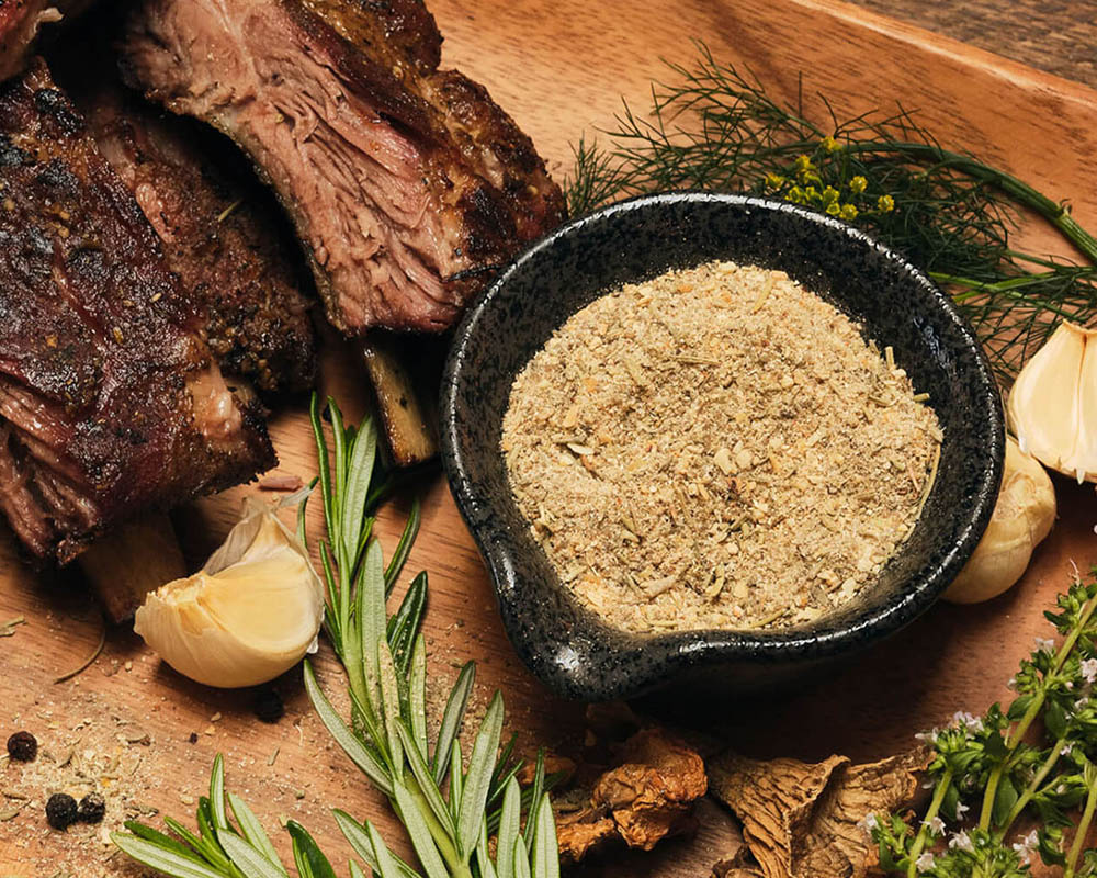 Dry spice mix in a bowl on a platter with cooked meat and fresh herbs.