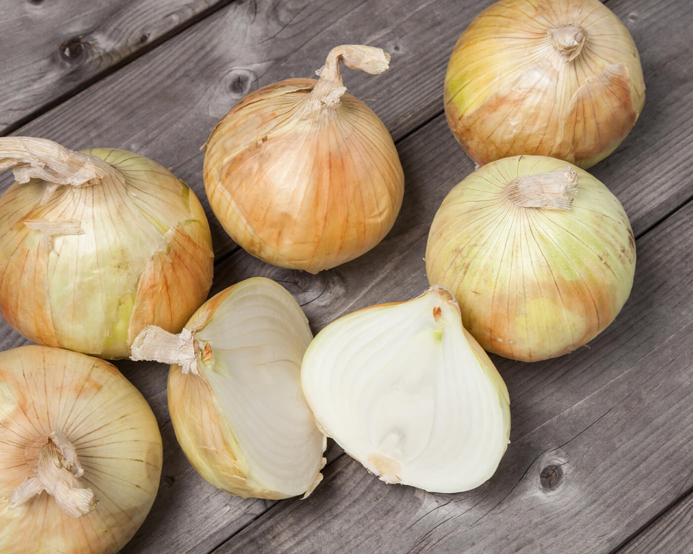 five whole onions and one onion cut in half on a wood surface