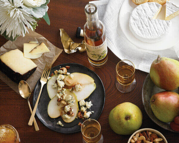 Festive table setting with cheese, wine, and sliced pear.