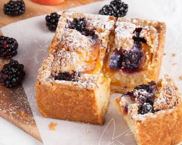 Bakewell tart cut into pieces with blackberries on top.