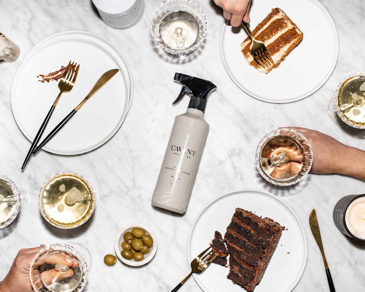 Bottle of cleaning spray on a kitchen table with plates of food surrounding it.