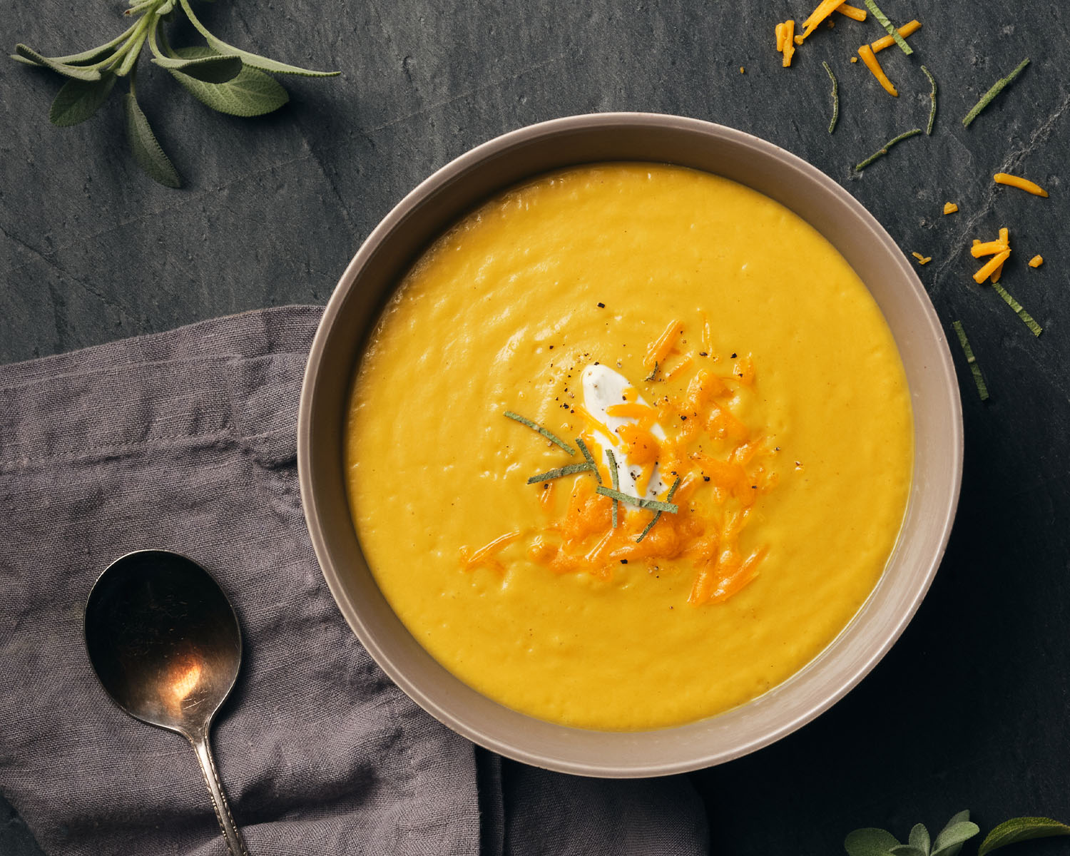 Bowl of warm golden butternut squash soup on a slate background with herbs.