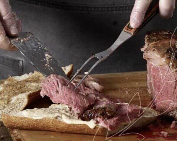 Chef slicing prime rib onto a sandwich.