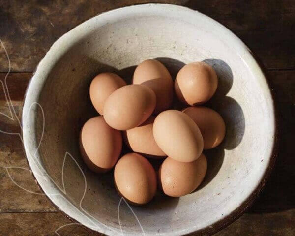 White bowl filled with brown eggs on a wooden table.