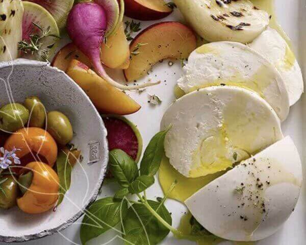 Slices of mozzarella on a tray with fresh fruit and vegetables.