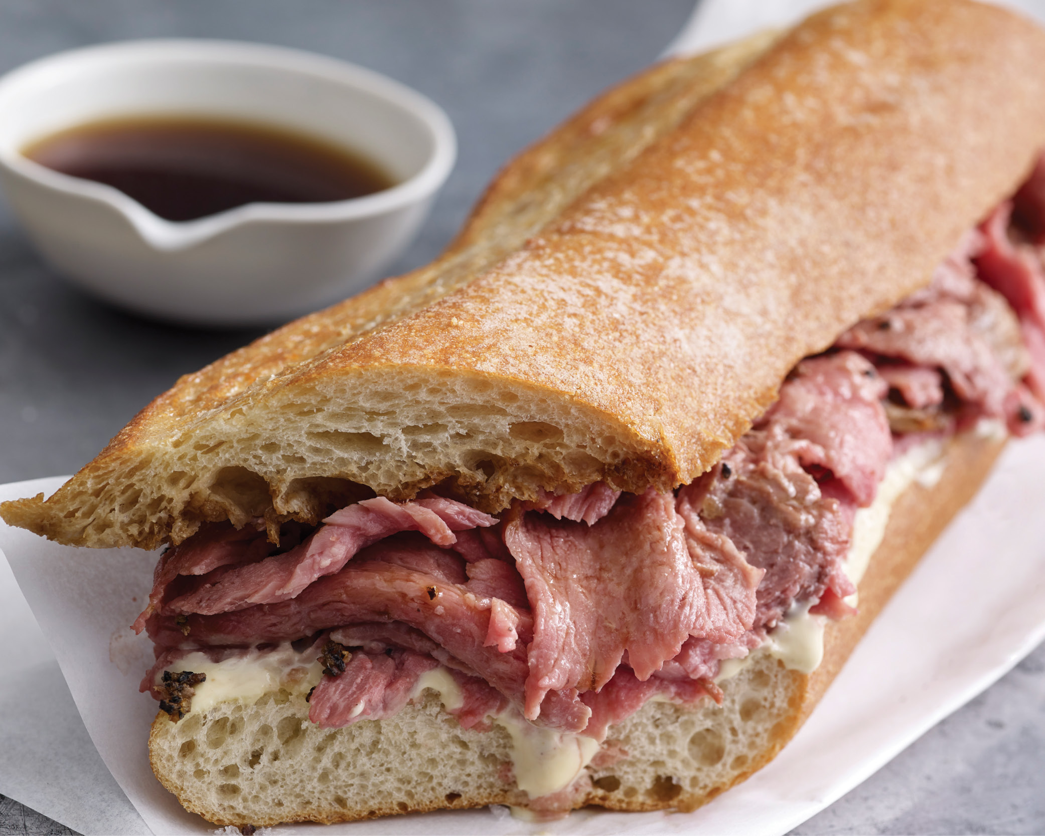 Close up shot of prime rib sandwich with au jus in the background.