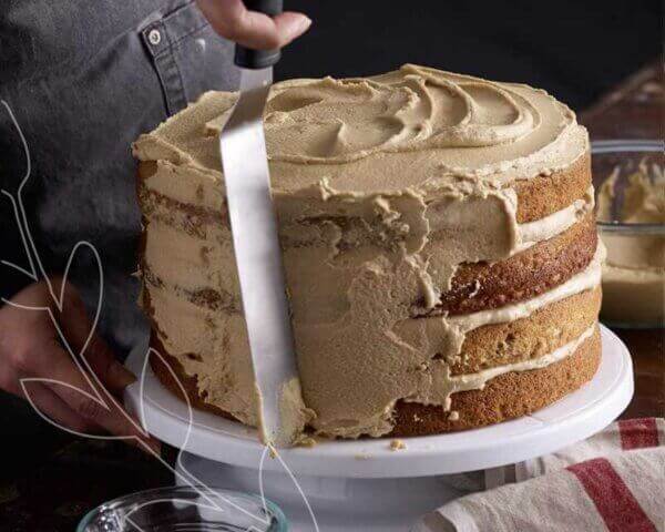 Baker frosting a hummingbird cake on a stand.